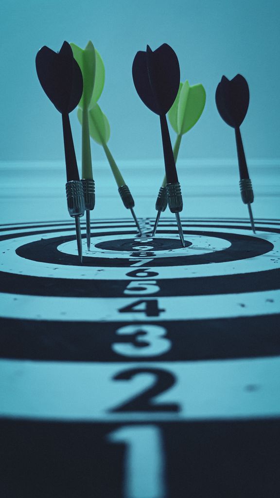 Close-up view of darts hitting a bullseye on a target board, symbolizing precision and focus.